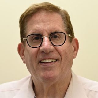 Portrait d'un homme aux lunettes rondes et chemise claire, nommé au Prix de l'Opticien International de l'Année 2025