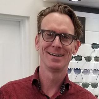 Portrait d'un homme debout dans une boutique d'optique, nommé au Prix de l'Opticien International de l'Année 2025