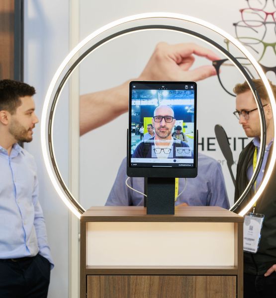 2 men talking at SILMO Paris while a third tries on glasses virtually